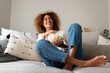 © Daniel - Young multiracial woman laughing watching tv at home sitting on the sofa eating popcorn.