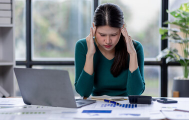 Portrait of tired young business Asian woman work with documents tax laptop computer in office. Sad, unhappy, Worried, Depression, or employee life stress concept
