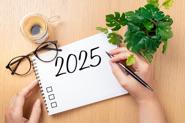 Wall Mural - New year resolutions 2025 on desk. 2025 goals - hands and notebook, coffee cup, plant on wooden table. Resolutions, plan, goals, action,  idea concept. New Year 2025 resolutions, copy space