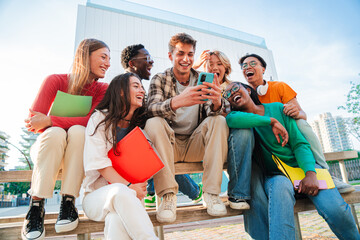 group of diverse students sitting outdoors, laughing and using a cellphone together, enjoying social