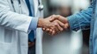 © ifoto - A close-up of two hands shaking, one in a white doctor's coat and stethoscope with a blue tie, the other man wearing a jeans shirt.