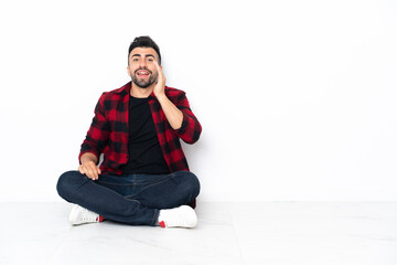 Young handsome man sitting on the floor shouting with mouth wide open