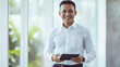 © Alina Tymofieieva - Professional man smiling while holding a tablet in a bright office environment during daytime