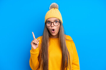 Young caucasian woman wearing winter clothes isolated on blue background intending to realizes the solution while lifting a finger up