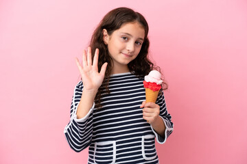 Little caucasian girl holding an ice cream isolated on pink background saluting with hand with happy expression