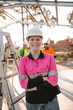 © Austockphoto - A young woman apprentice on construction site with arms crossed standing and smiling at the camera