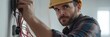© gunzexx png and bg - A focused electrician in a hard hat works diligently on wiring within a building, exemplifying dedication and precision in electrical construction tasks.