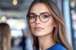 © SerPak - Young woman wears stylish glasses and looks confidently at the camera while standing in a modern room. Sunlight fills the space, highlighting her features and creating a warm atmosphere as people chat
