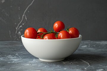 A white bowl filled with ripe red cherry tomatoes on a vine, on a grey background.