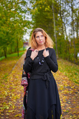 Beautiful woman in black dress and necklace walking in autumn forest. Relaxation concept