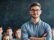 © Al the Magician - Young male teacher with glasses and beard, standing confidently with arms crossed in front of a classroom and blackboard, students in the background.