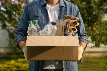 Wall Mural - Recycling. Man holding cardboard box with different garbage outdoors, closeup