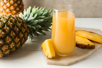 Tasty pineapple juice in glass and fresh fruits on white wooden table against grey background, closeup