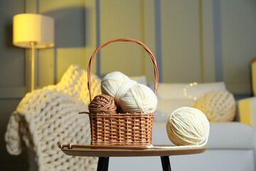 Sticker - Wicker basket with colorful yarns and knitting needles on coffee table in cozy room