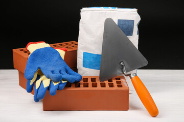 Wall Mural - Cement powder in bag, gloves, trowel and red bricks on white wooden table. Building materials and construction tools