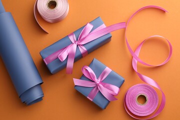 Wall Mural - Beautiful gift boxes with pink bows, ribbons and roll of wrapping paper on orange background, flat lay