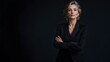 © Jittapon - Portrait of a solemn and contemplative middle aged woman dressed in a sleek black pantsuit standing against a plain charcoal background with dramatic studio lighting