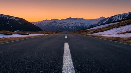 Empty road leading through snowy mountain range at sunset.