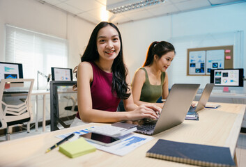 two young asian businesswomen are working on laptops in a modern office, analyzing financial data an