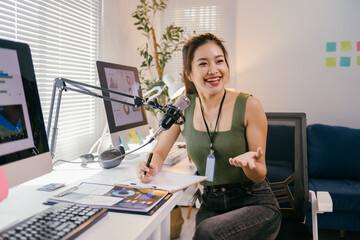 Smiling asian businesswoman records a podcast in her home office, discussing reports with enthusiasm. The scene showcases a modern remote entrepreneur's success