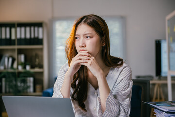 Young businesswoman sitting at her desk with her hands clasped and a worried expression on her face, feeling the pressure of a difficult job