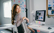 © PaeGAG - Asian businesswoman is sitting at her desk in her office, working on her computer. She is smiling over her shoulder at the camera