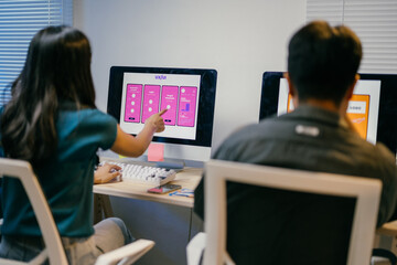 Two web designers are working in the office, analyzing the user interface of a mobile phone application they are developing