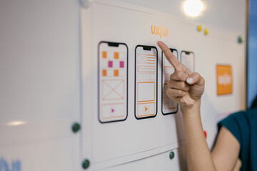 Web designer is pointing at a whiteboard and showing the different stages of development of a mobile application. She is explaining the process to her team