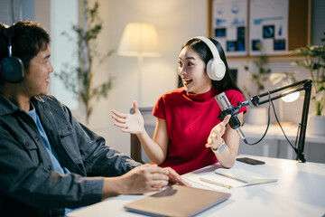 Two young asian podcasters wearing headphones are recording audio for their channel, discussing and laughing during their podcast