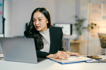 Young businesswoman is working on a project using a laptop and analyzing charts at her desk in a bright modern office