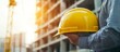© logitech - A construction worker holds a yellow hard hat in front of a partially built structure.
