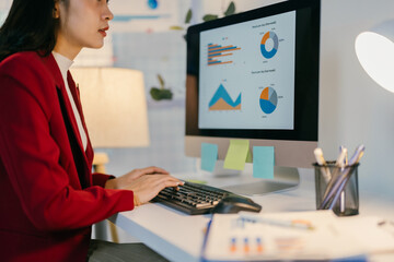 Wall Mural - Businesswoman is working at her desk, analyzing financial data displayed on her computer screen. The office environment is bright and modern