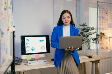 Confident businesswoman in modern office with laptop, surrounded by technology and data, exudes success through strategic planning