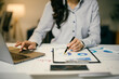 © Parichat - Businesswoman is working late, using a laptop and analyzing financial charts with a pen in hand, illuminated by warm office lighting