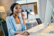 © PaeGAG - African american businesswoman is smiling while talking on a headset and working on her computer at her bright and modern office