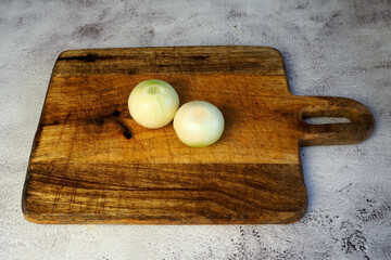 On the gray marble table lies a wooden dark brown board with two whole onions peeled from the husk. side view kitchen. copy space