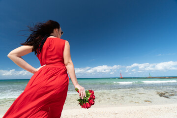 Beautiful young woman with blond long hair in red fluttering dress is near retro car convertible on the coastline of azure caribbean sea	
