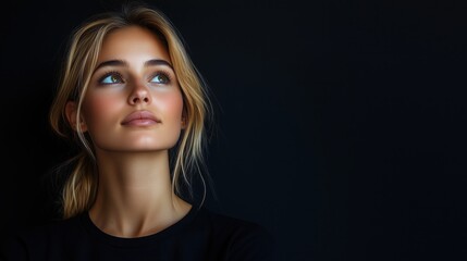 Portrait of a young woman with a serious face. Attractive blonde woman thoughtfully looks up, thinking about something. Person isolated on black background, copy space.