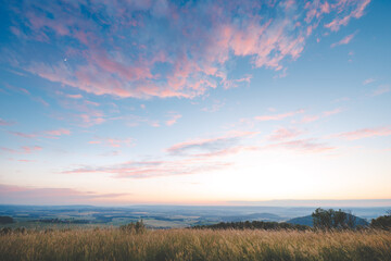 Breathtaking view of the Czech countryside at sunset with a serene sky painted in soft pink and blue hues. The peaceful landscape stretches over vast fields, capturing the beauty of nature