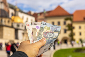 Fototapete - Money from Oman held in the hand of a tourist in front of the castle in Krakow. Traveling in Poland and Eastern European countries. Trendy travel destinations for tourists from Arab countries