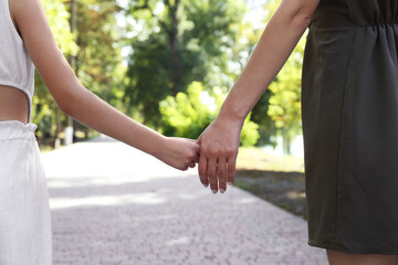 Wall Mural - Mother and daughter holding hands in park, closeup