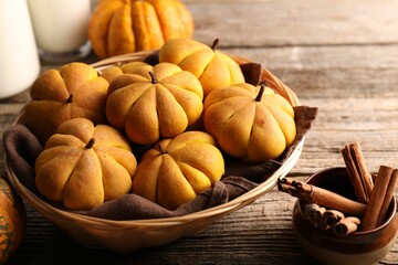 Poster - Wicker basket with tasty pumpkin shaped buns and cinnamon sticks on wooden table, closeup