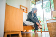 © Odua Images - In a bright, airy room, a young woman comfortably sits on her bed, tying her shoes with ease