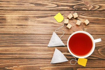 Cup of tea with tea bags and sugar cubes on brown wooden table