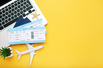 Airline boarding passes with passports, laptop, airplane model and green plant on yellow background