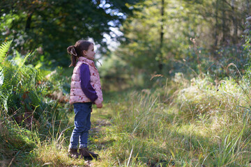 Little beautiful girl in a hoodie and vest against the background of a dark autumn forest. Concept of a happy childhood in nature