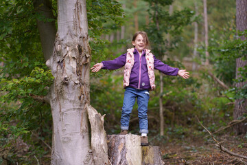 Little beautiful girl in a hoodie and vest against the background of a dark autumn forest. Concept of a happy childhood in nature