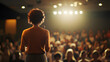 © Jonah - A nonbinary employee giving a keynote speech at a company conference standing on stage with a large audience of colleagues listening promoting inclusion and diversity.