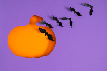 Halloween background. Stylish and creative Halloween background with cut out orange pumpkin silhouette on purple paper with paper bats. Flat lay. Banner.