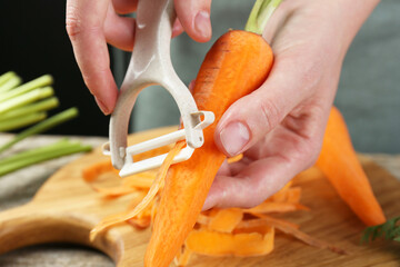 Poster - Woman peeling fresh carrot at wooden table, closeup